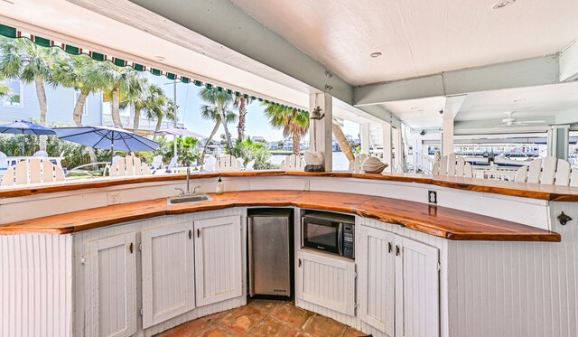 kitchen featuring plenty of natural light, butcher block countertops, black microwave, and a sink