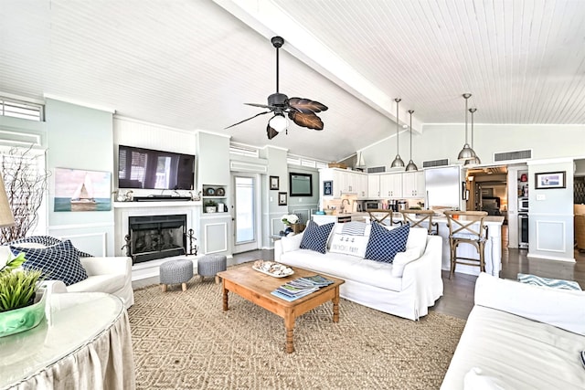 living area with visible vents, a fireplace with raised hearth, a ceiling fan, lofted ceiling with beams, and dark wood-type flooring