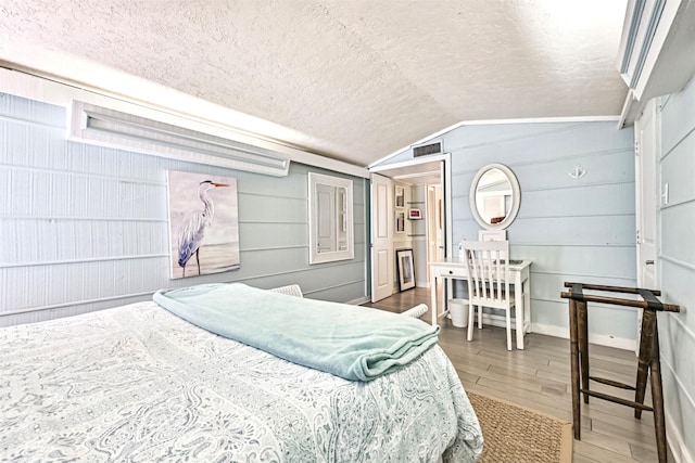 bedroom featuring lofted ceiling, a textured ceiling, wood finished floors, and visible vents