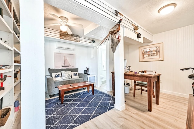 sitting room with baseboards, a wall unit AC, ceiling fan, wood finished floors, and a textured ceiling