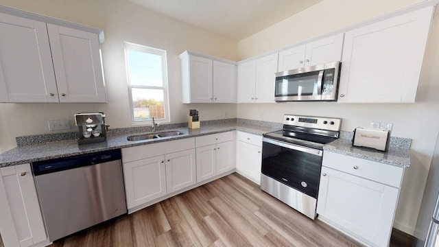 kitchen featuring light wood-style flooring, appliances with stainless steel finishes, white cabinetry, a sink, and light stone countertops