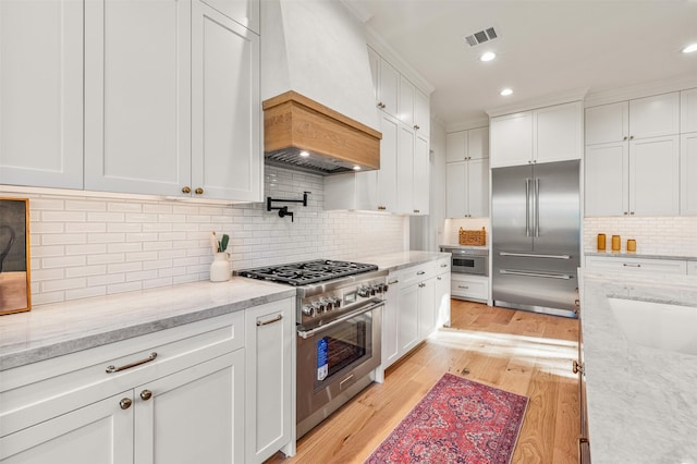 203 Munford St, Houston, TX 77008 - kitchen with custom exhaust hood, visible vents, high quality appliances, backsplash, and white cabinets