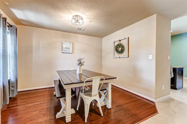 dining space with visible vents, baseboards, a textured ceiling, and wood finished floors