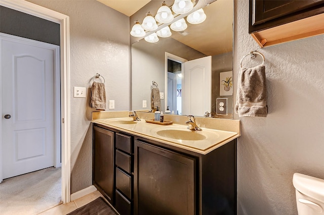 full bath with a sink, toilet, double vanity, and a textured wall