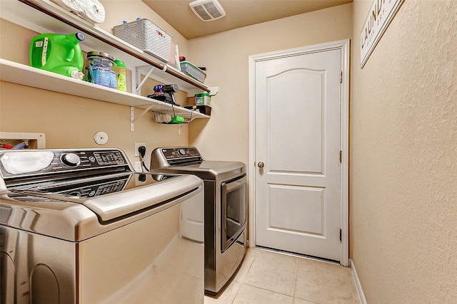 clothes washing area with visible vents, washer and clothes dryer, light tile patterned floors, baseboards, and laundry area