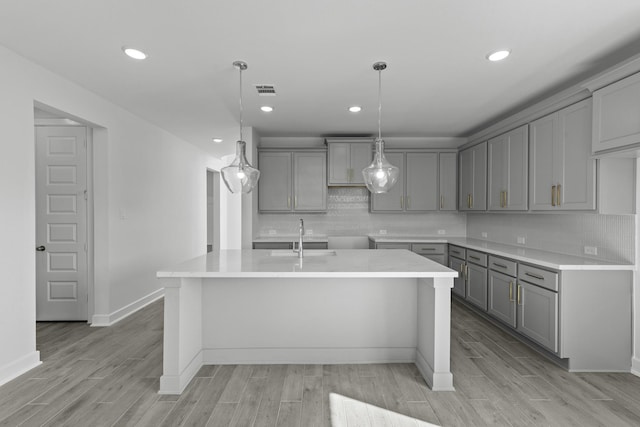 kitchen with light wood-style flooring, gray cabinets, and a kitchen island with sink