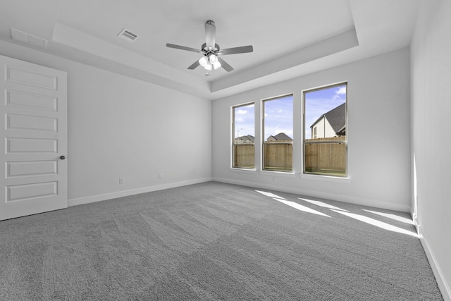 empty room with visible vents, baseboards, ceiling fan, carpet, and a tray ceiling