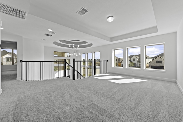 carpeted spare room featuring a chandelier, a raised ceiling, visible vents, and baseboards