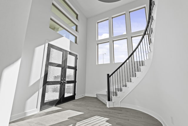 foyer entrance featuring wood finished floors, a towering ceiling, baseboards, stairs, and french doors