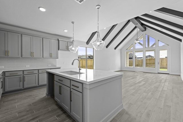 kitchen featuring wood finish floors, tasteful backsplash, light countertops, gray cabinetry, and a sink