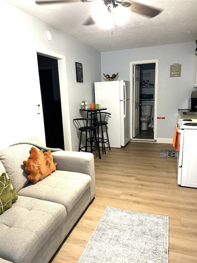 living room featuring baseboards, light wood-style flooring, and a ceiling fan