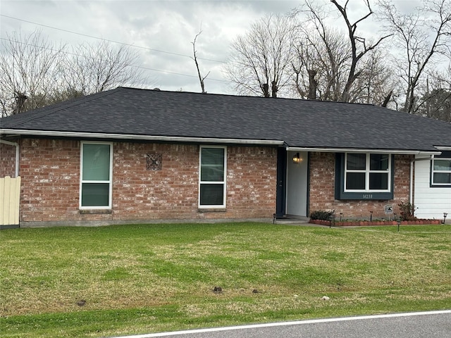 ranch-style house featuring brick siding, a front yard, and roof with shingles