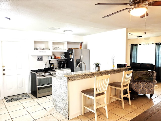 kitchen with light tile patterned floors, ceiling fan, appliances with stainless steel finishes, a peninsula, and a kitchen bar