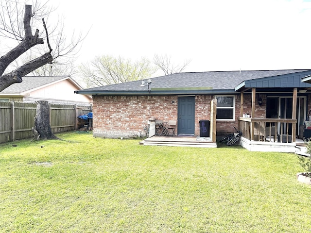 back of property with brick siding, roof with shingles, fence, and a yard