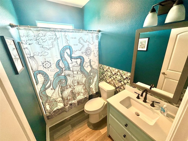 bathroom with wainscoting, toilet, wood finished floors, vanity, and tile walls