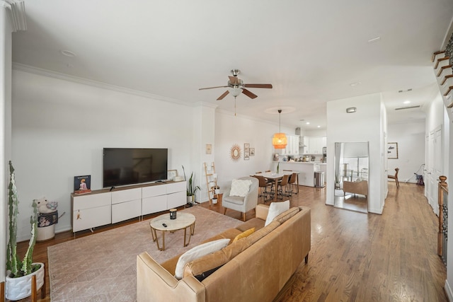 living room featuring ceiling fan, crown molding, baseboards, and wood finished floors