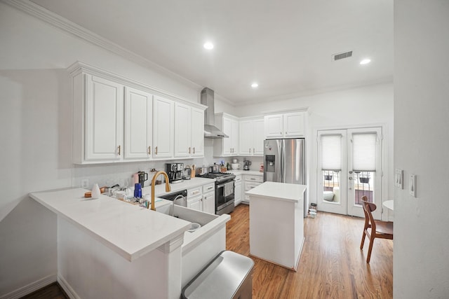 kitchen with light wood-style flooring, stainless steel appliances, light countertops, wall chimney range hood, and white cabinetry