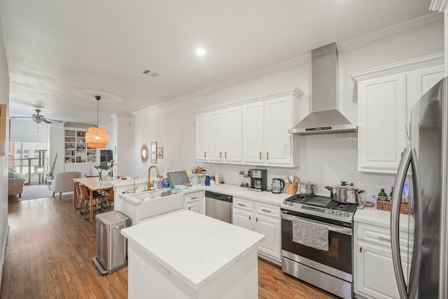 kitchen with light wood finished floors, wall chimney exhaust hood, a kitchen island, ornamental molding, and stainless steel appliances