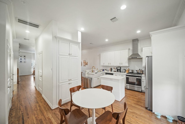 kitchen with visible vents, appliances with stainless steel finishes, a center island, light countertops, and wall chimney range hood