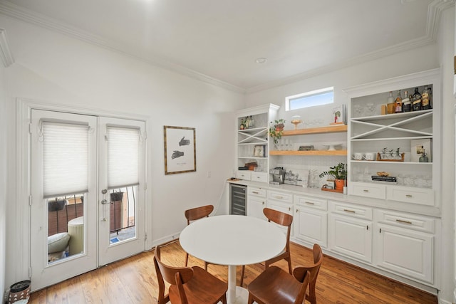 dining space with beverage cooler, a bar, ornamental molding, and light wood-style floors