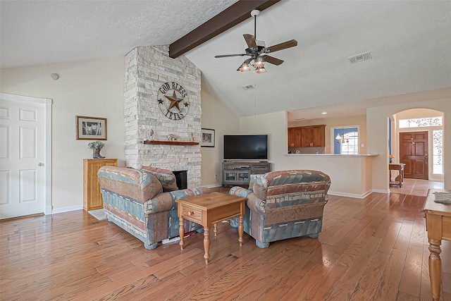 living room with visible vents, arched walkways, wood-type flooring, a stone fireplace, and beam ceiling