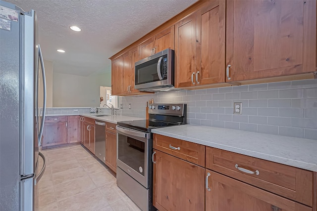 kitchen with appliances with stainless steel finishes, light tile patterned flooring, a sink, and brown cabinets