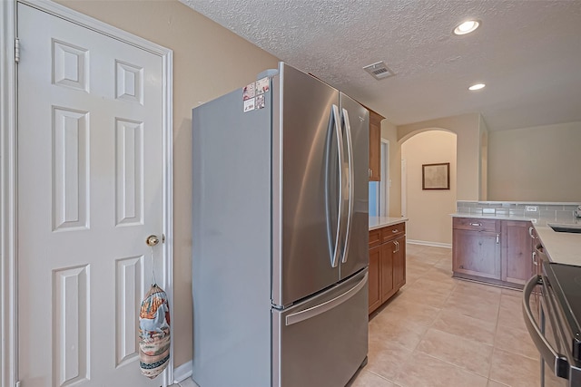 kitchen with light tile patterned floors, arched walkways, electric stove, freestanding refrigerator, and light countertops