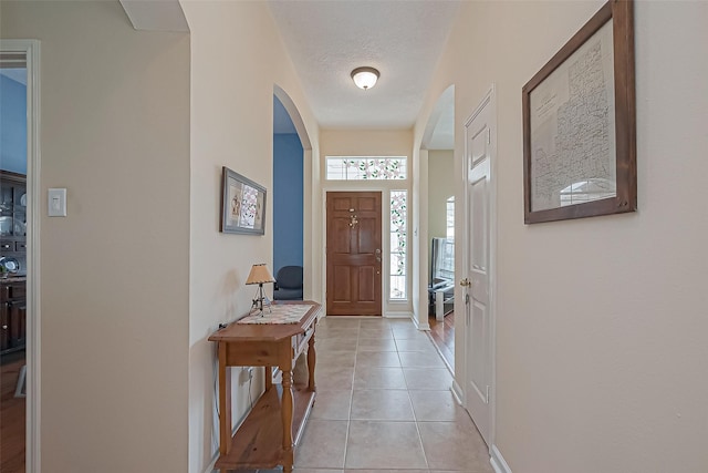 foyer featuring a textured ceiling, light tile patterned flooring, arched walkways, and baseboards