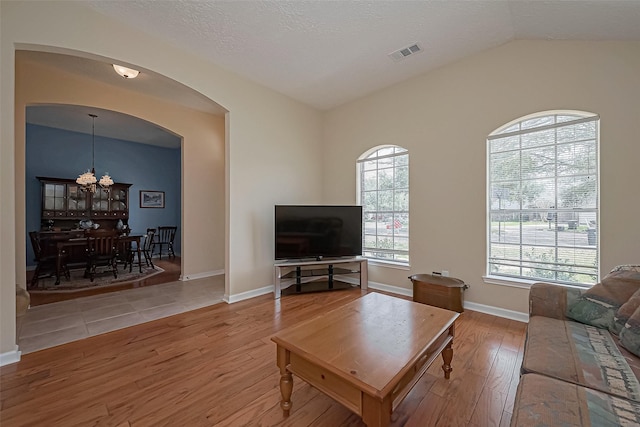 living room featuring lofted ceiling, visible vents, wood finished floors, a chandelier, and baseboards