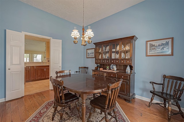 dining room featuring baseboards, a textured ceiling, light wood-type flooring, and an inviting chandelier