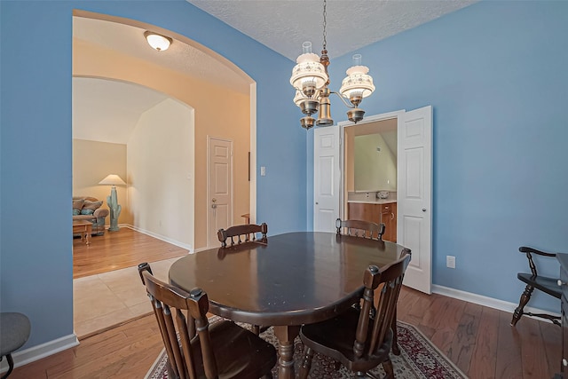 dining space with baseboards, arched walkways, wood finished floors, an inviting chandelier, and a textured ceiling