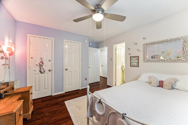 bedroom featuring baseboards, dark wood-style flooring, two closets, and ceiling fan