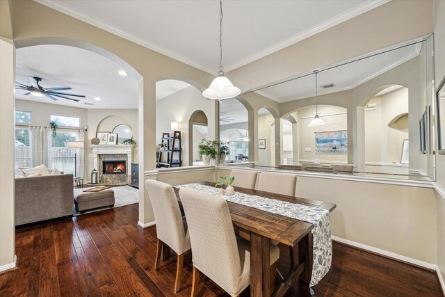 dining space with a ceiling fan, baseboards, a fireplace, ornamental molding, and dark wood-type flooring