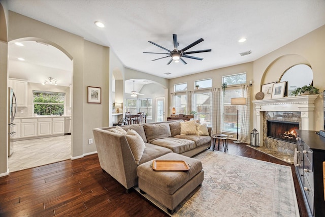 living area featuring a high end fireplace, visible vents, ceiling fan, dark wood finished floors, and arched walkways