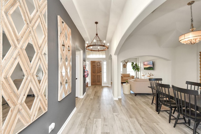 foyer entrance with arched walkways, a notable chandelier, a towering ceiling, light wood-style flooring, and baseboards