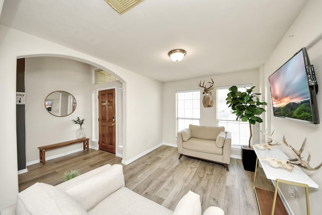 living area with light wood-type flooring, visible vents, arched walkways, and baseboards