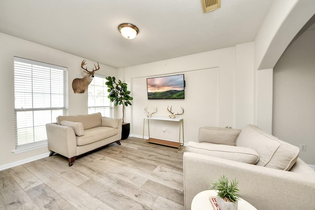 living room featuring light wood-type flooring, baseboards, visible vents, and arched walkways