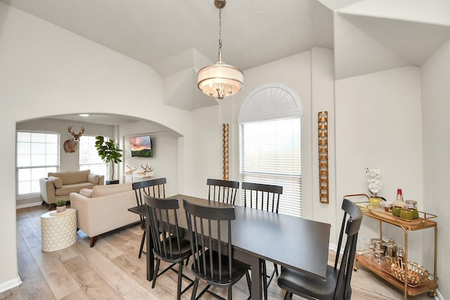 dining area featuring arched walkways, lofted ceiling, an inviting chandelier, light wood-type flooring, and baseboards