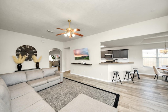 living room with light wood finished floors, visible vents, arched walkways, baseboards, and ceiling fan with notable chandelier