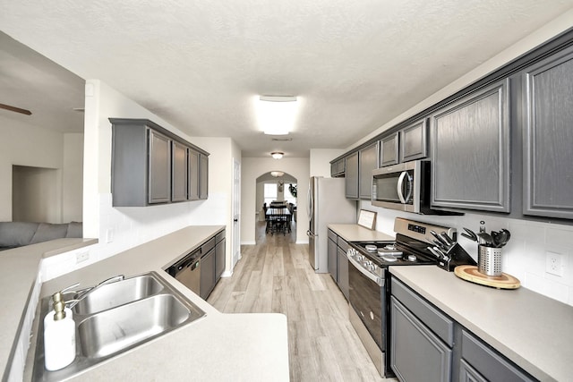 kitchen with arched walkways, appliances with stainless steel finishes, a sink, a textured ceiling, and light wood-type flooring