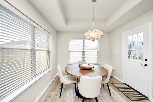 dining room featuring light wood-style floors, a tray ceiling, baseboards, and an inviting chandelier