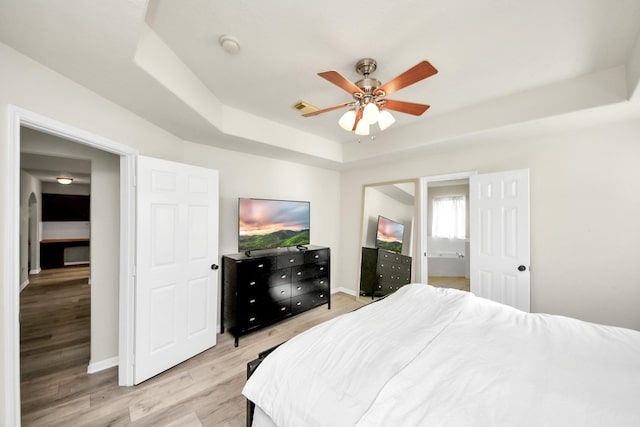 bedroom featuring light wood finished floors, baseboards, visible vents, ceiling fan, and a tray ceiling