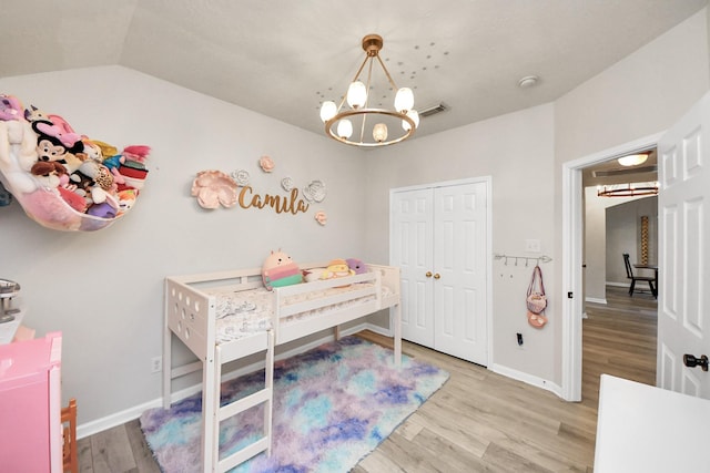 bedroom with baseboards, visible vents, wood finished floors, vaulted ceiling, and a chandelier