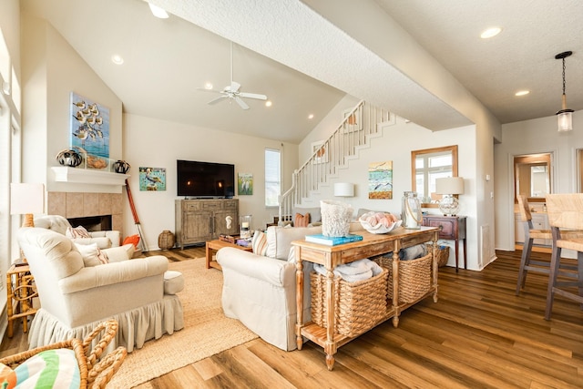 living room with a tile fireplace, wood finished floors, stairs, vaulted ceiling, and recessed lighting