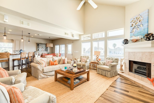 living room with ceiling fan, light wood-style flooring, a tiled fireplace, and visible vents