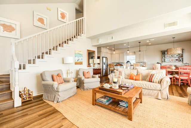 living area featuring stairway, light wood-type flooring, a towering ceiling, and visible vents