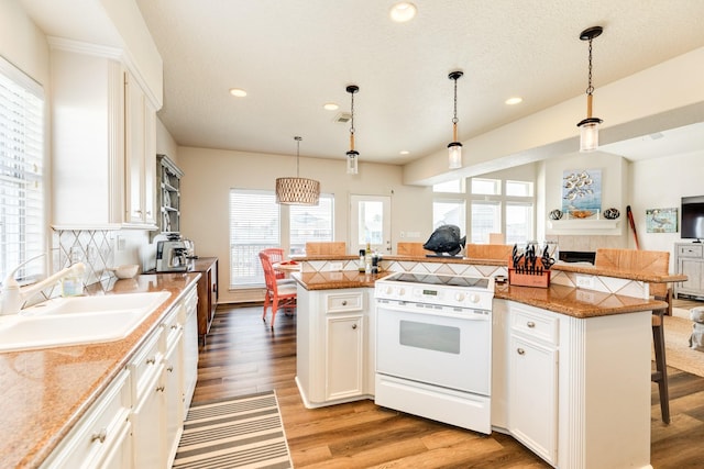 kitchen with white electric stove, light wood finished floors, tasteful backsplash, a sink, and a kitchen bar