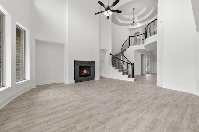 unfurnished living room featuring plenty of natural light, light wood-style flooring, stairs, and a glass covered fireplace