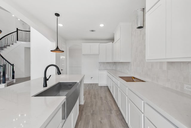 kitchen with light wood finished floors, visible vents, decorative light fixtures, white cabinetry, and backsplash