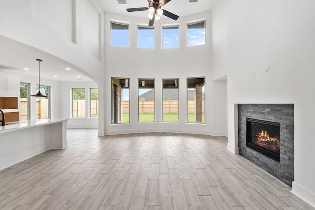 unfurnished living room with baseboards, ceiling fan, wood tiled floor, a fireplace, and a sink